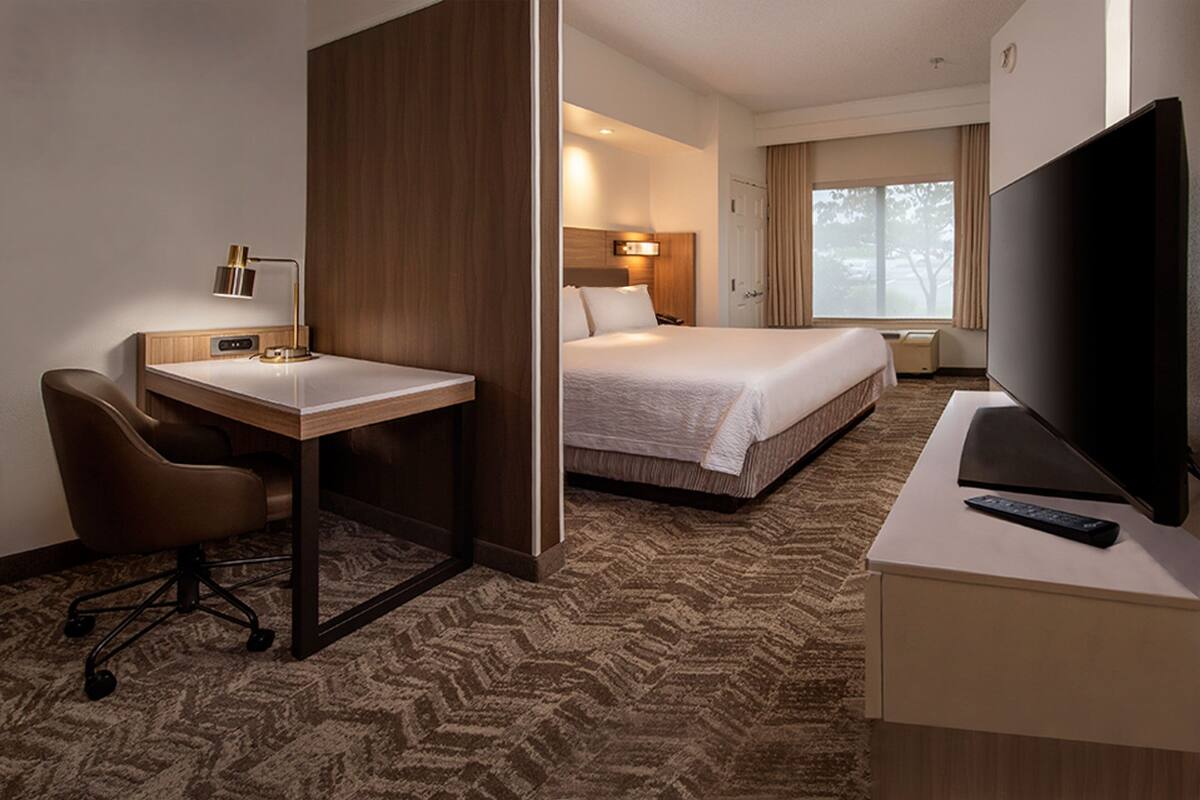 Habitación de hotel con cama, escritorio con silla, televisor y ventana con cortinas.