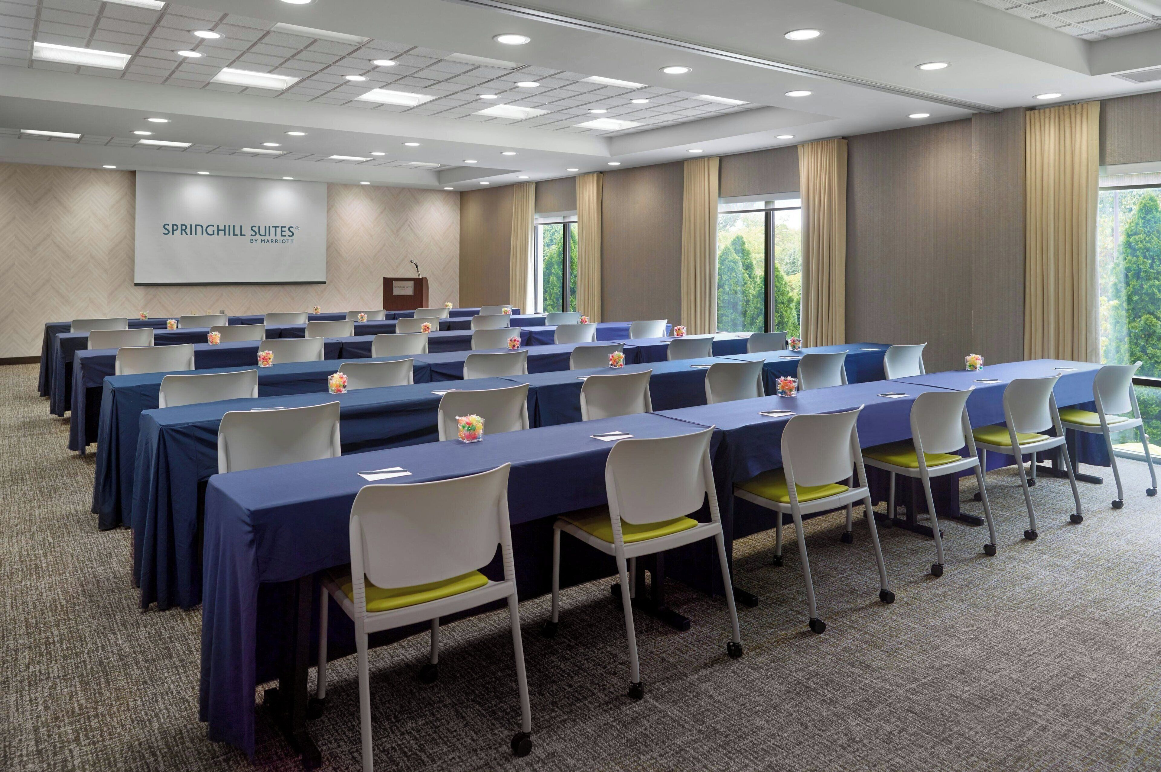 A conference room with rows of tables and chairs, a podium, and a screen displaying 'SPRINGHILL SUITES BY HARRIOT'.