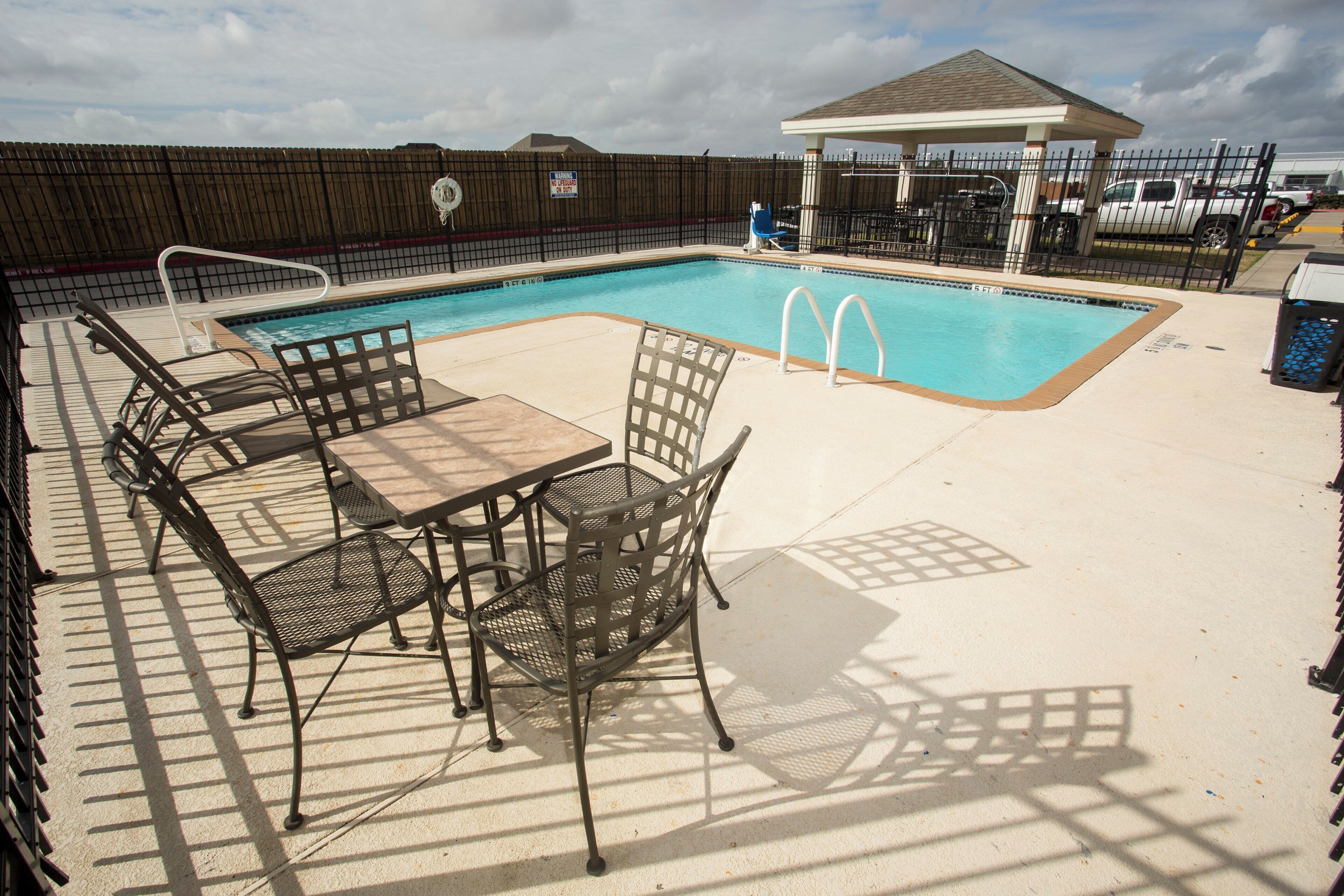A swimming pool with a fenced area, lounge chairs, and a covered seating area.