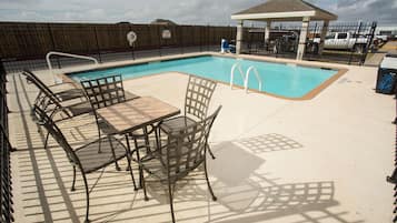 A swimming pool with a fenced area, lounge chairs, and a covered seating area.