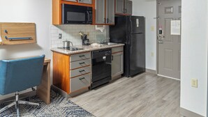 Een compacte keuken met houten kastjes, een zwarte koelkast, een magnetron en een koffiezetapparaat.