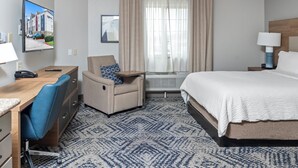 Een hotelkamer met een bed, bureau, stoel en een groot raam met gordijnen.