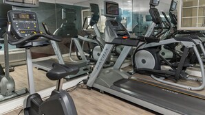 Een sportschool met diverse fitnessapparaten, waaronder loopbanden en hometrainers, en een spiegelwand.