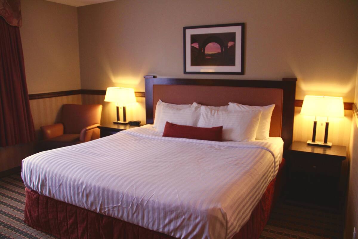 A hotel room with a large bed, two bedside tables with lamps, a chair, and a framed picture on the wall.
