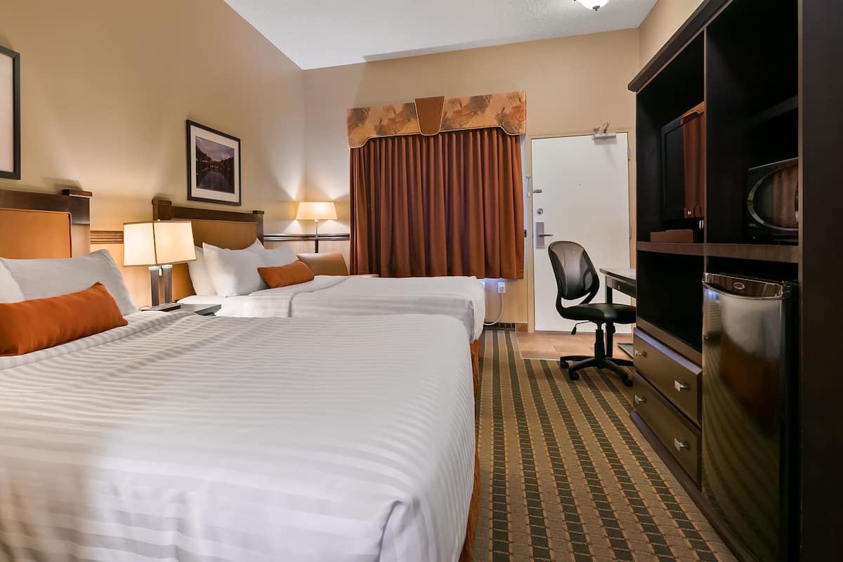 A hotel room with two beds, a desk, a chair, a television, and a refrigerator.