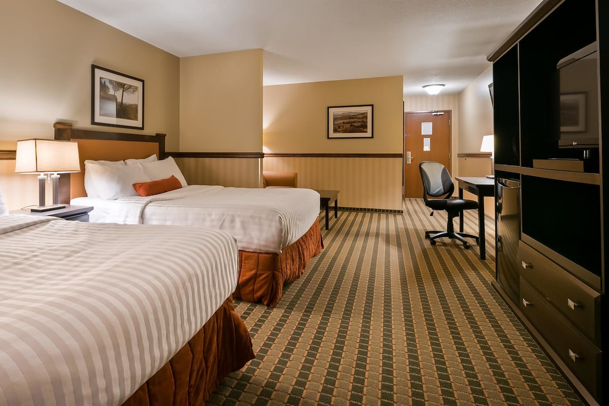 A hotel room with two beds, a desk, a chair, and a television.