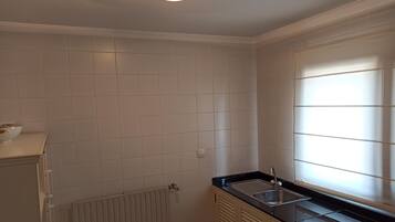 Cozinha com azulejos brancos, bancada preta, pia e janela com persianas.