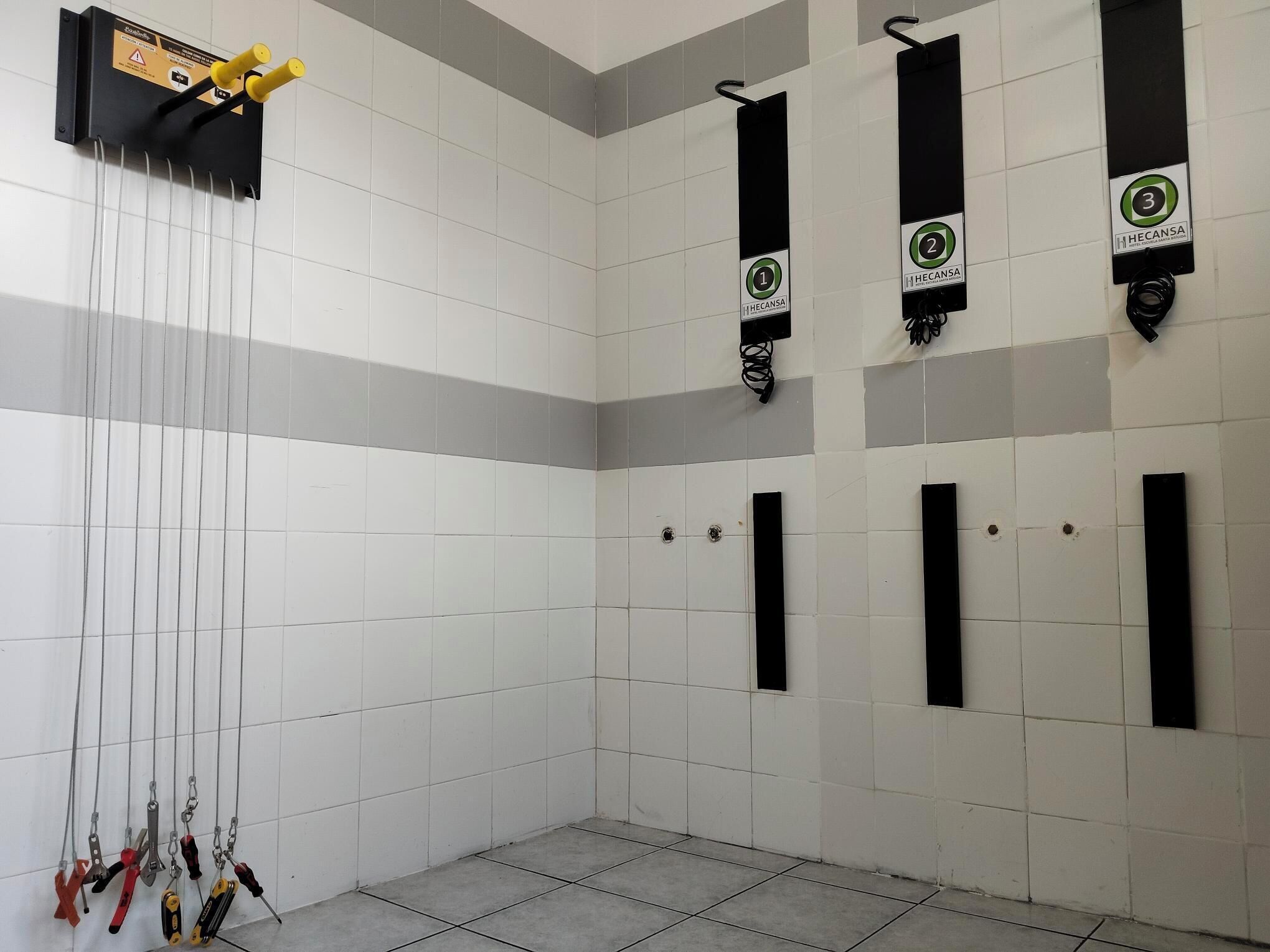Un baño con baldosas, varios toalleros, un lavamanos y un juego de herramientas colgadas en la pared.