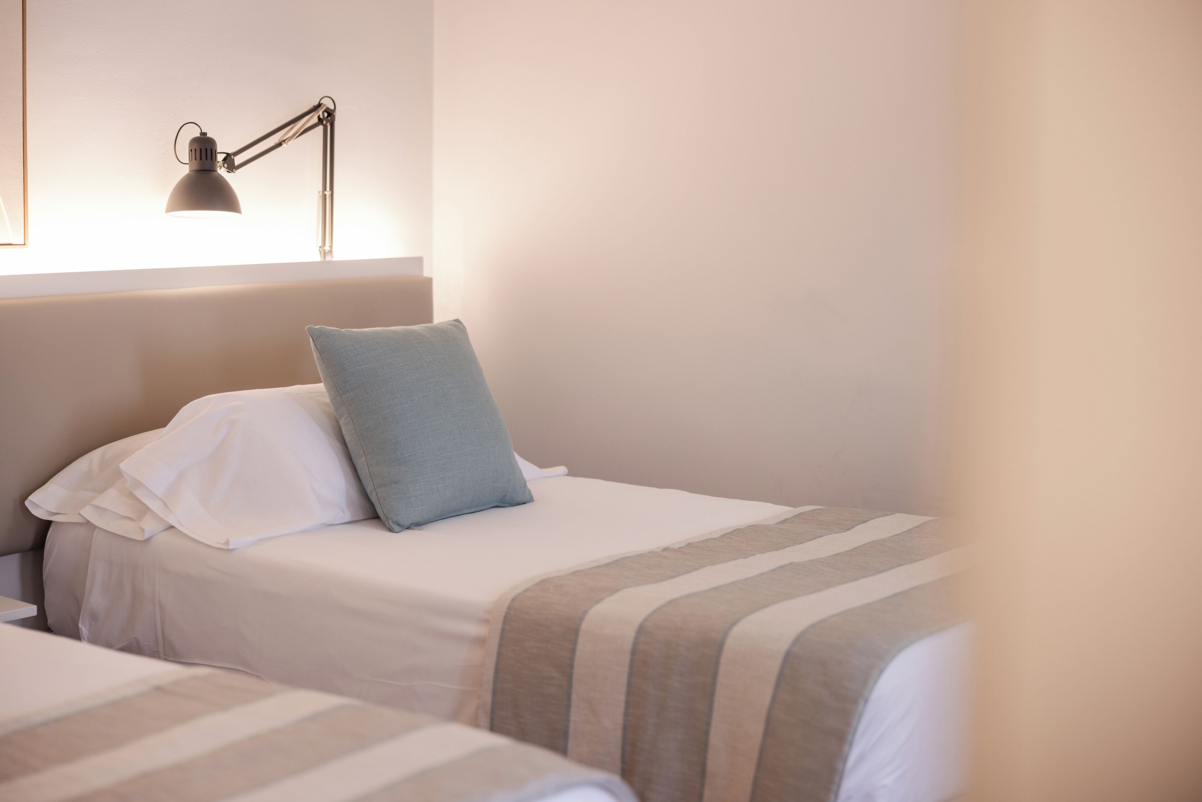 A hotel room with two beds, a bedside lamp, and a window.