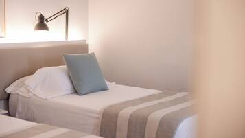 A hotel room with two beds, a bedside lamp, and a window.