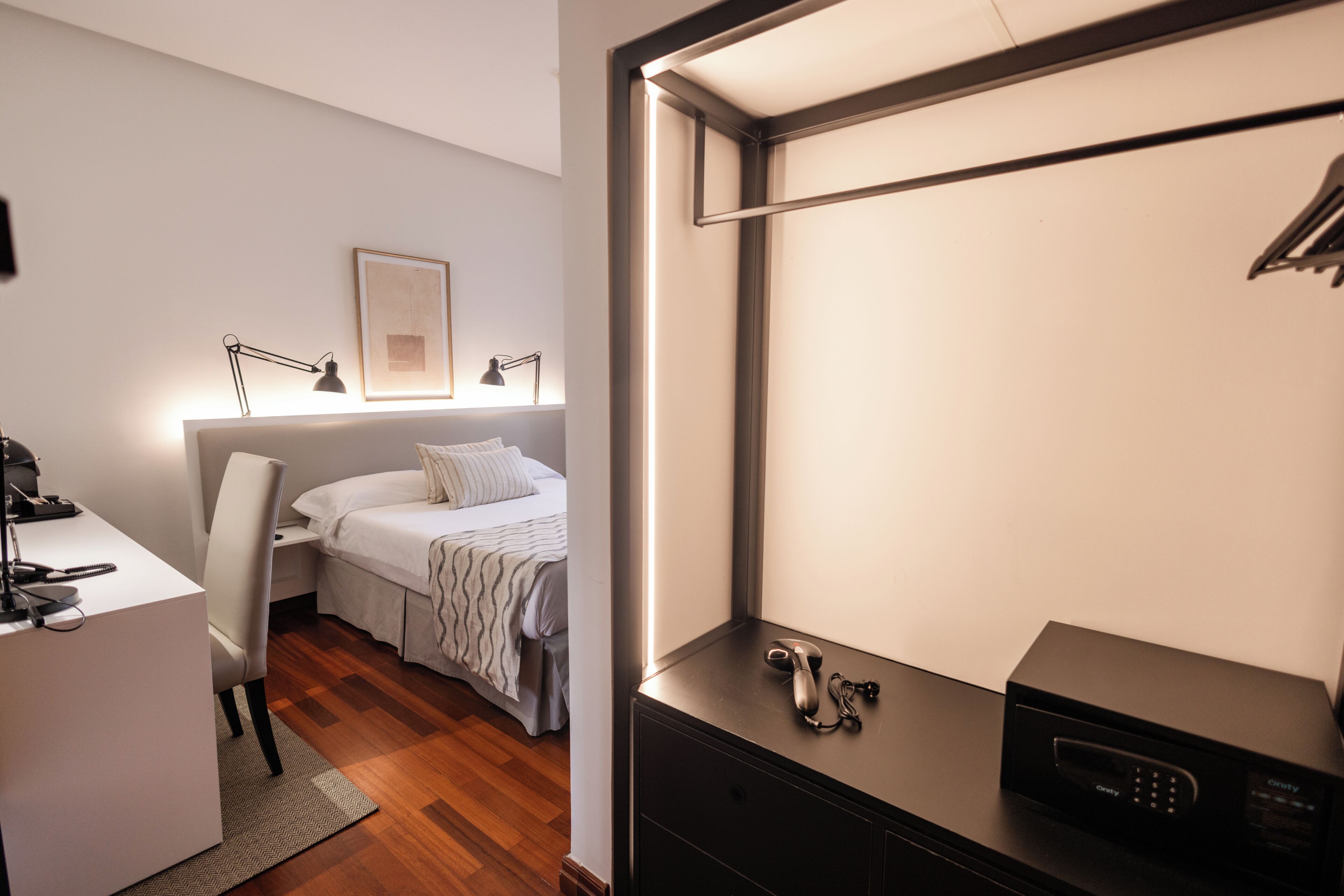 Een moderne hotelkamer met een bed, nachtkastje, bureau, stoel en een zwart tv-meubel.