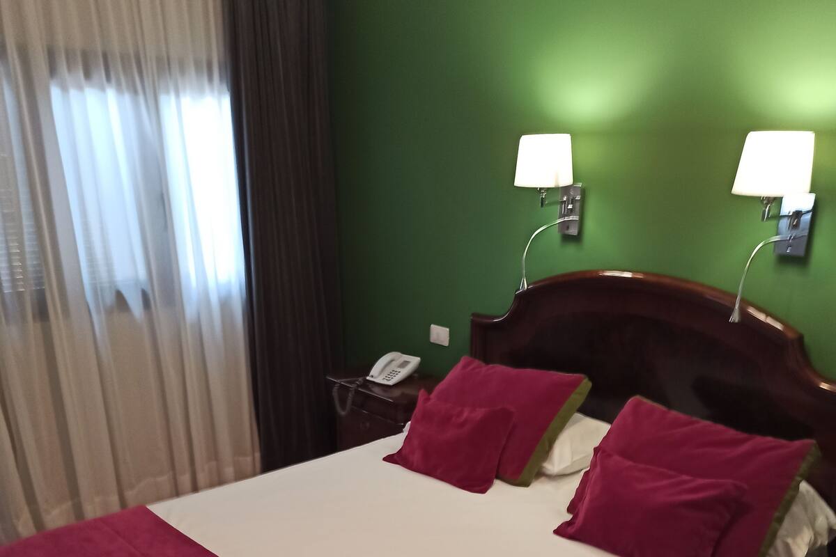 A hotel room with a large bed, two bedside lamps, a telephone, and a green wall.