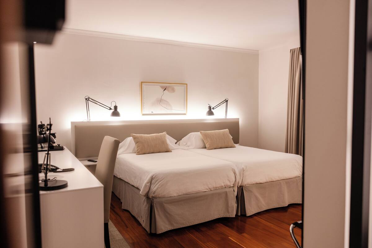 A double bed with two bedside tables, a desk with a lamp, and a framed picture on the wall.