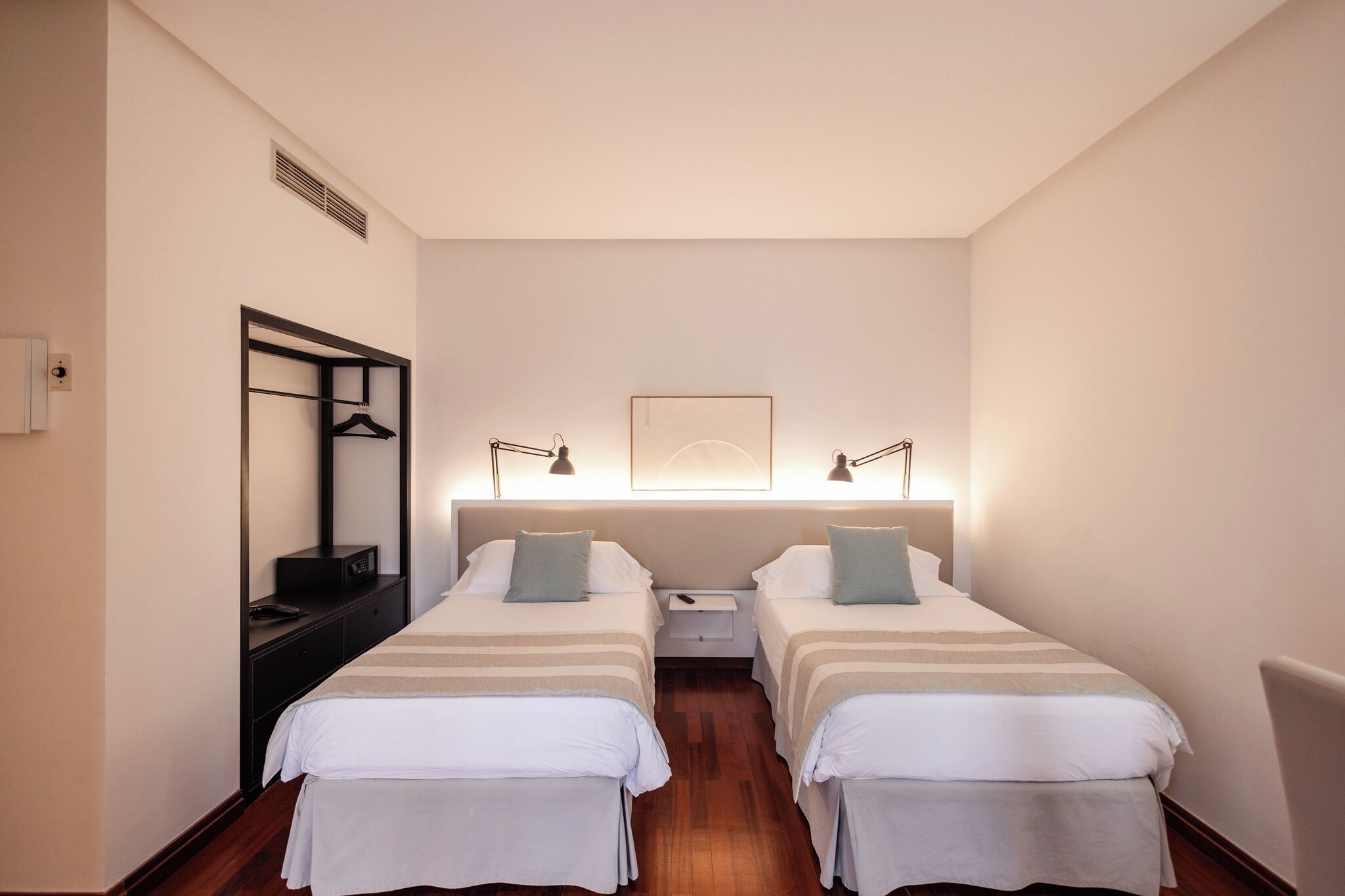 Une chambre d’hôtel avec deux lits, une table de chevet, un miroir et une œuvre d’art accrochée au mur.