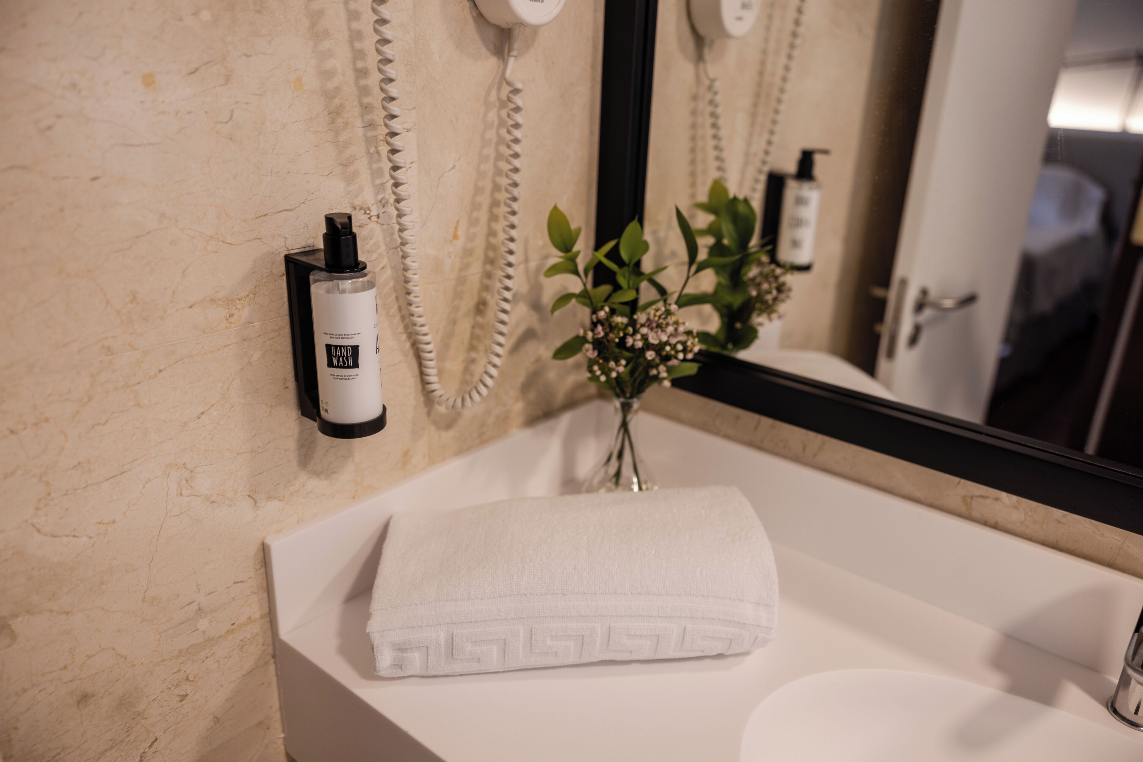 A bathroom with a white sink, a towel, a mirror, and a wall-mounted phone.