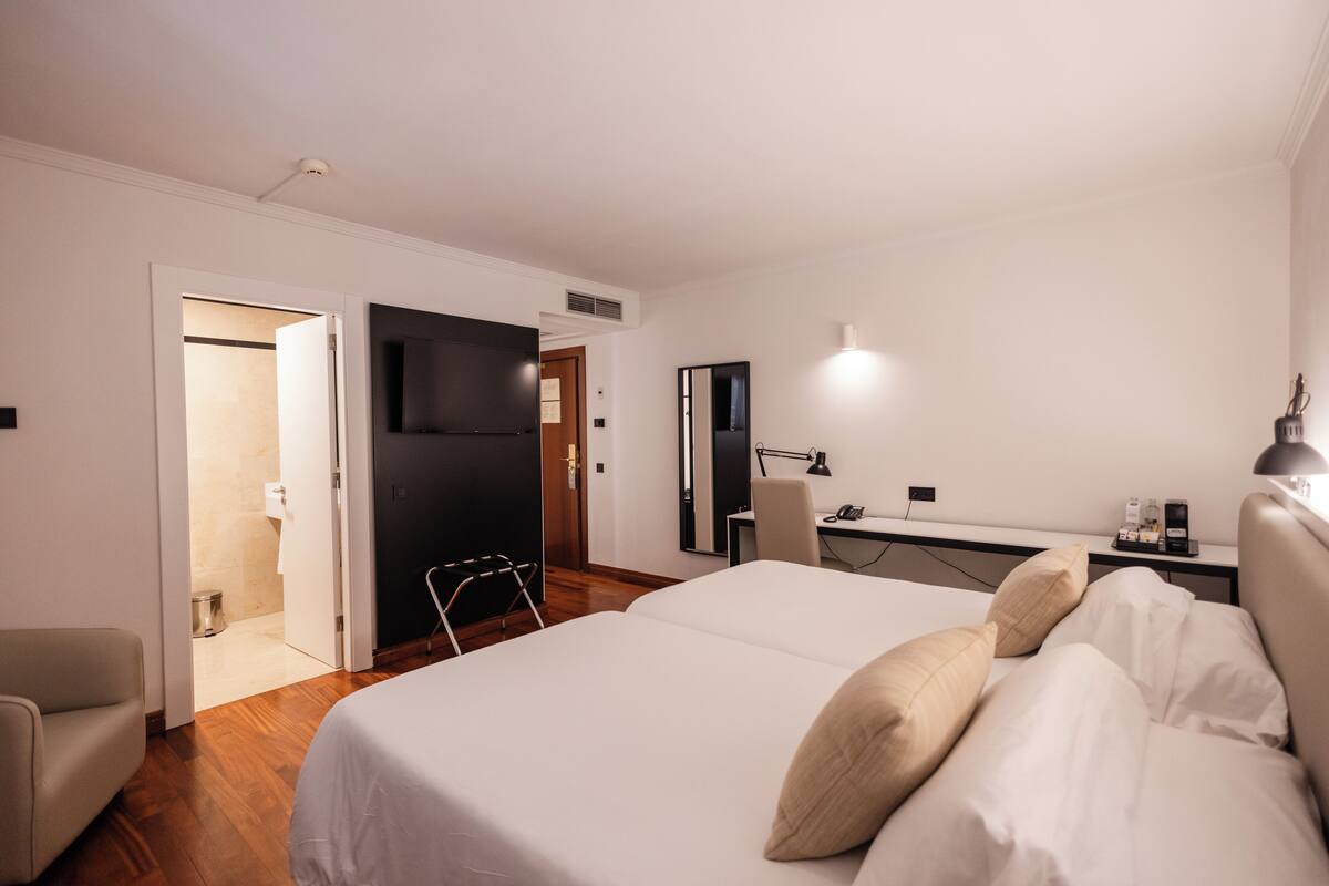 A hotel room with a bed, a desk, a chair, a TV, and a bathroom.