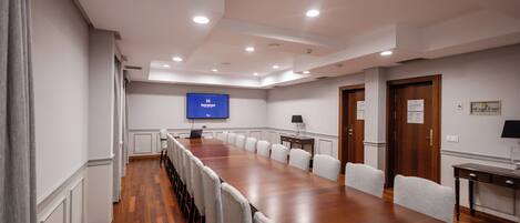 Un salón de conferencias con una larga mesa, sillas, una pantalla de televisión y una puerta de madera.