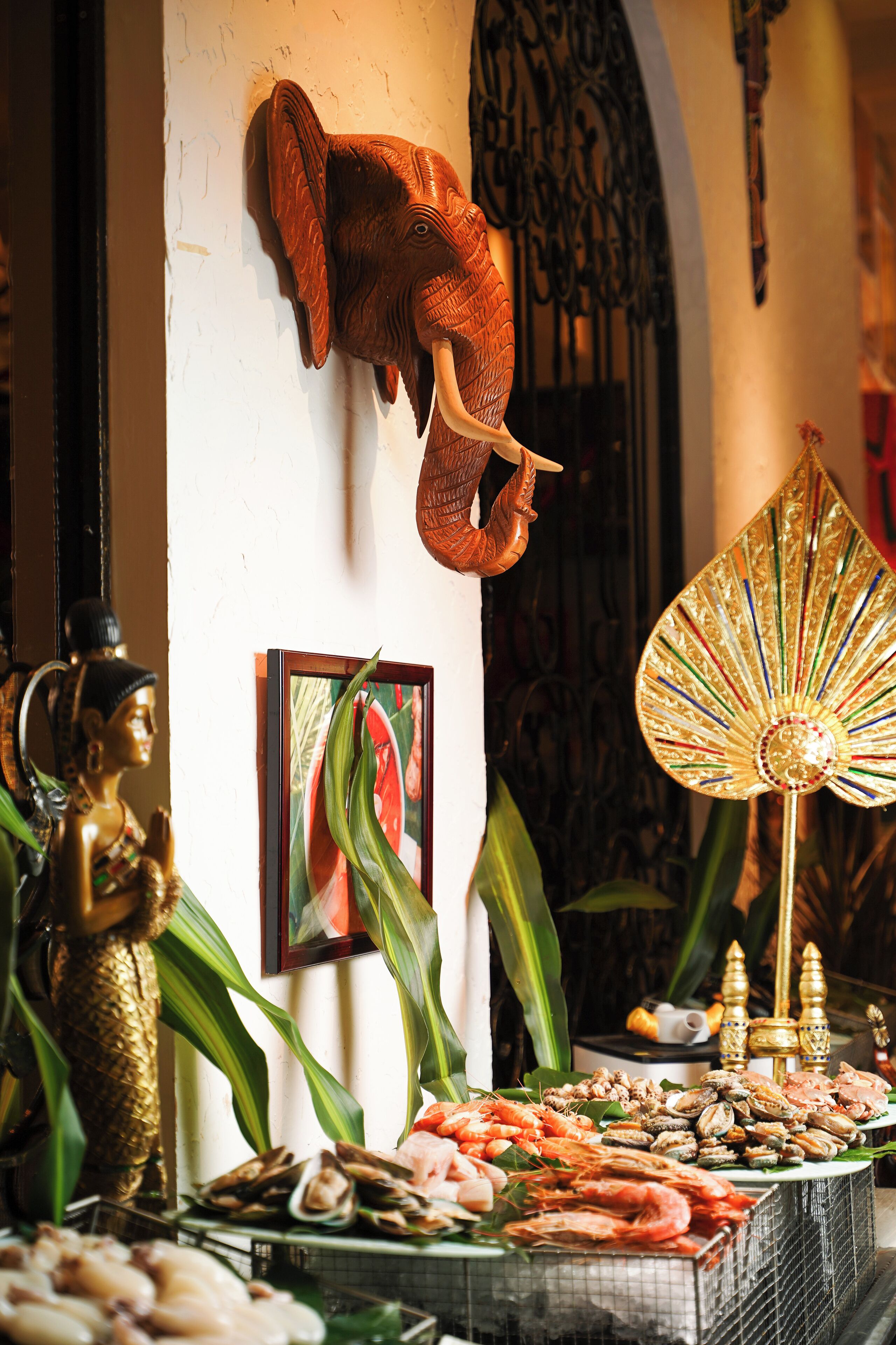 Eine Wandskulptur eines Elefanten, eine Buddha-Statue und verschiedene Meeresfrüchte sind auf einem Tisch angerichtet.