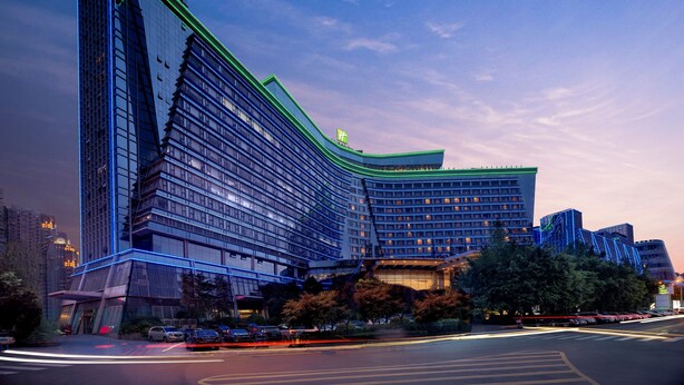 A modern hotel with a distinctive angular design, featuring multiple floors and a prominent green-lit entrance. - Holiday Inn Chengdu Century City-WestTower by IHG (Chengdu)