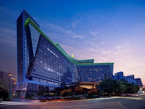 A modern hotel with a distinctive angular design, featuring multiple floors and a prominent green-lit entrance. - Holiday Inn Chengdu Century City-WestTower by IHG (Chengdu)