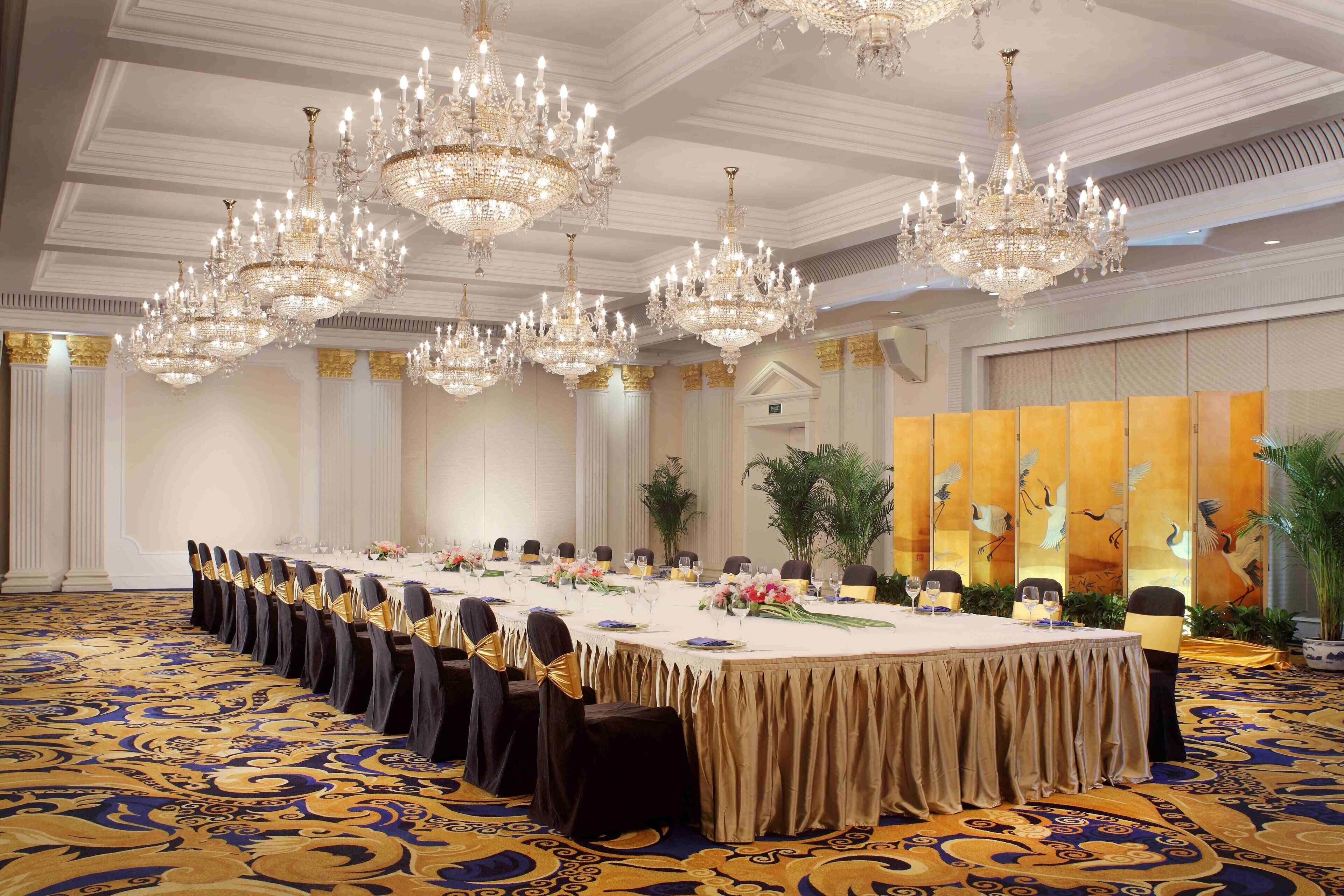 A formal dining room with a long table, multiple chandeliers, and a patterned carpet.