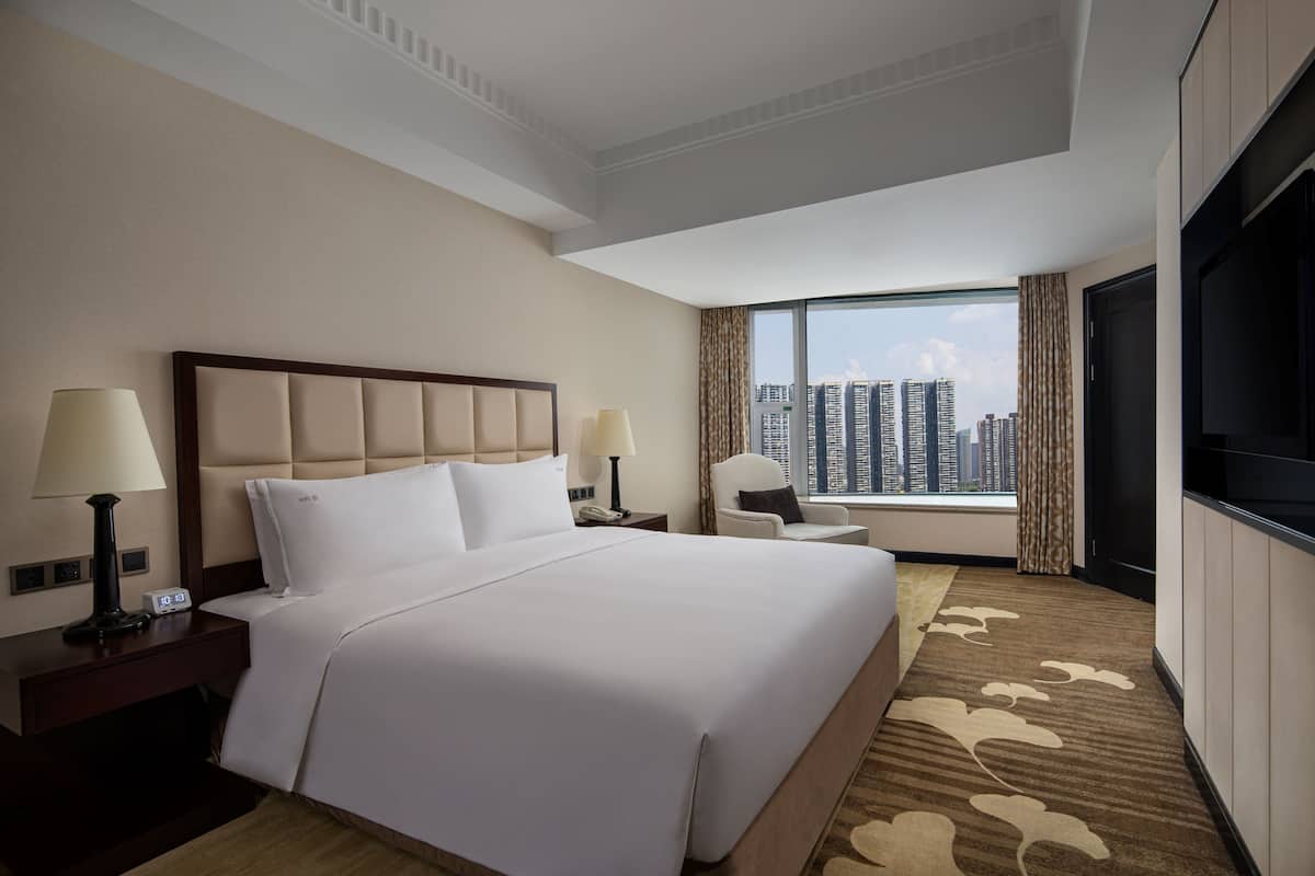A hotel room with a large bed, two bedside tables with lamps, a TV, and a view of the city skyline.