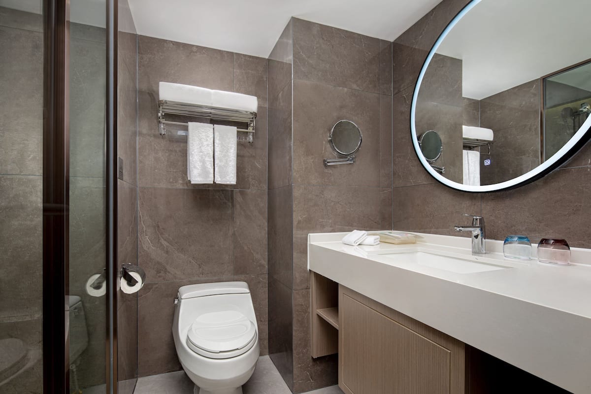 A modern bathroom with a toilet, a glass shower enclosure, a vanity with a mirror, and a towel rack.