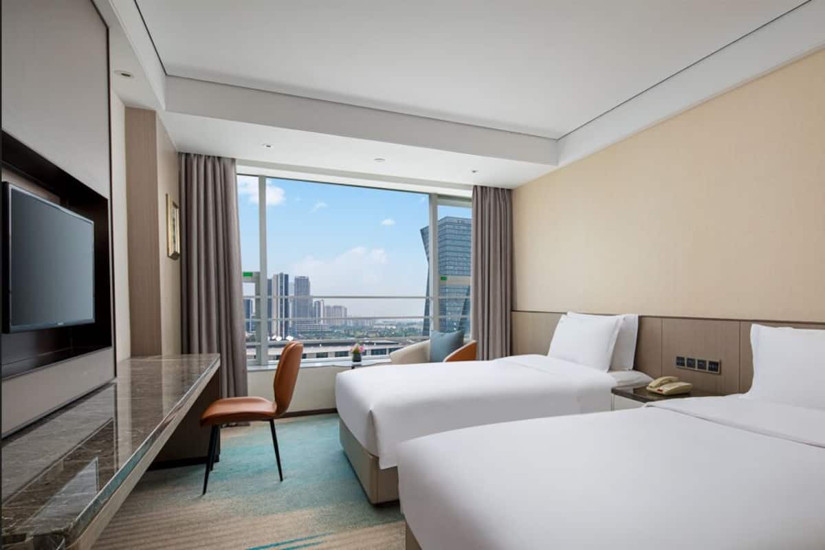 A hotel room with two beds, a TV, a desk, and a chair.