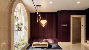Un vestíbulo moderno con un mostrador de recepción de mármol, una zona de estar con un banco tapizado oscuro y una lámpara colgante.