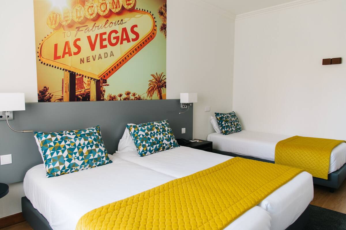 A hotel room with two beds, a neon sign on the wall, and a yellow bedspread.