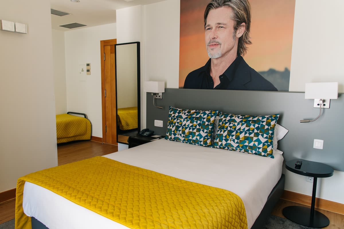 A hotel room with a large bed, a bedside table, a mirror, and a wall-mounted TV.