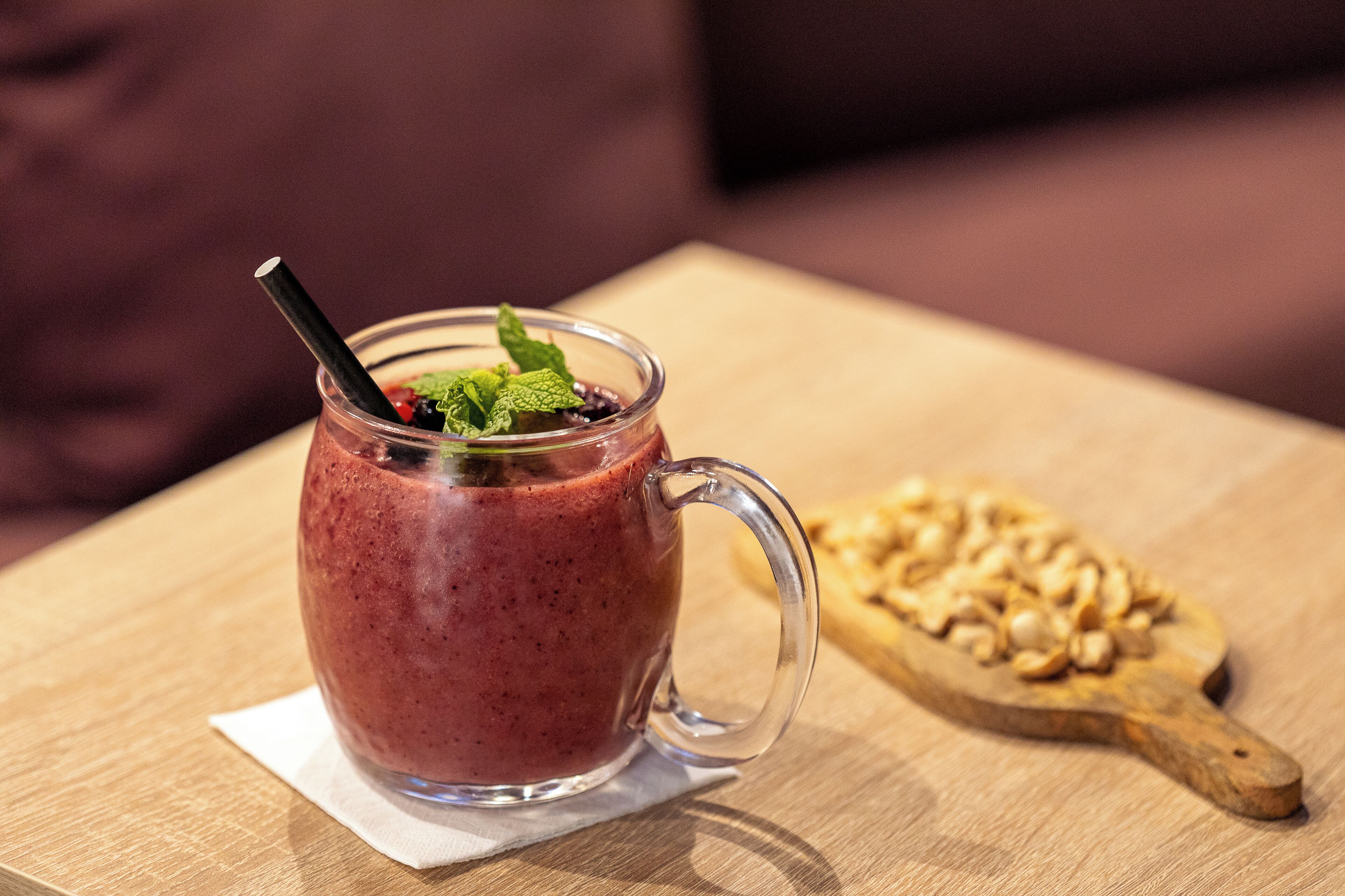 A glass mug with a straw and mint garnish on a wooden table.
