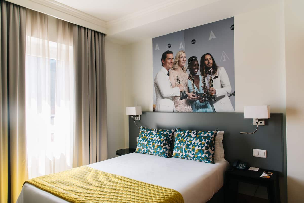 A hotel room with a bed, a nightstand, a lamp, and a wall-mounted picture.