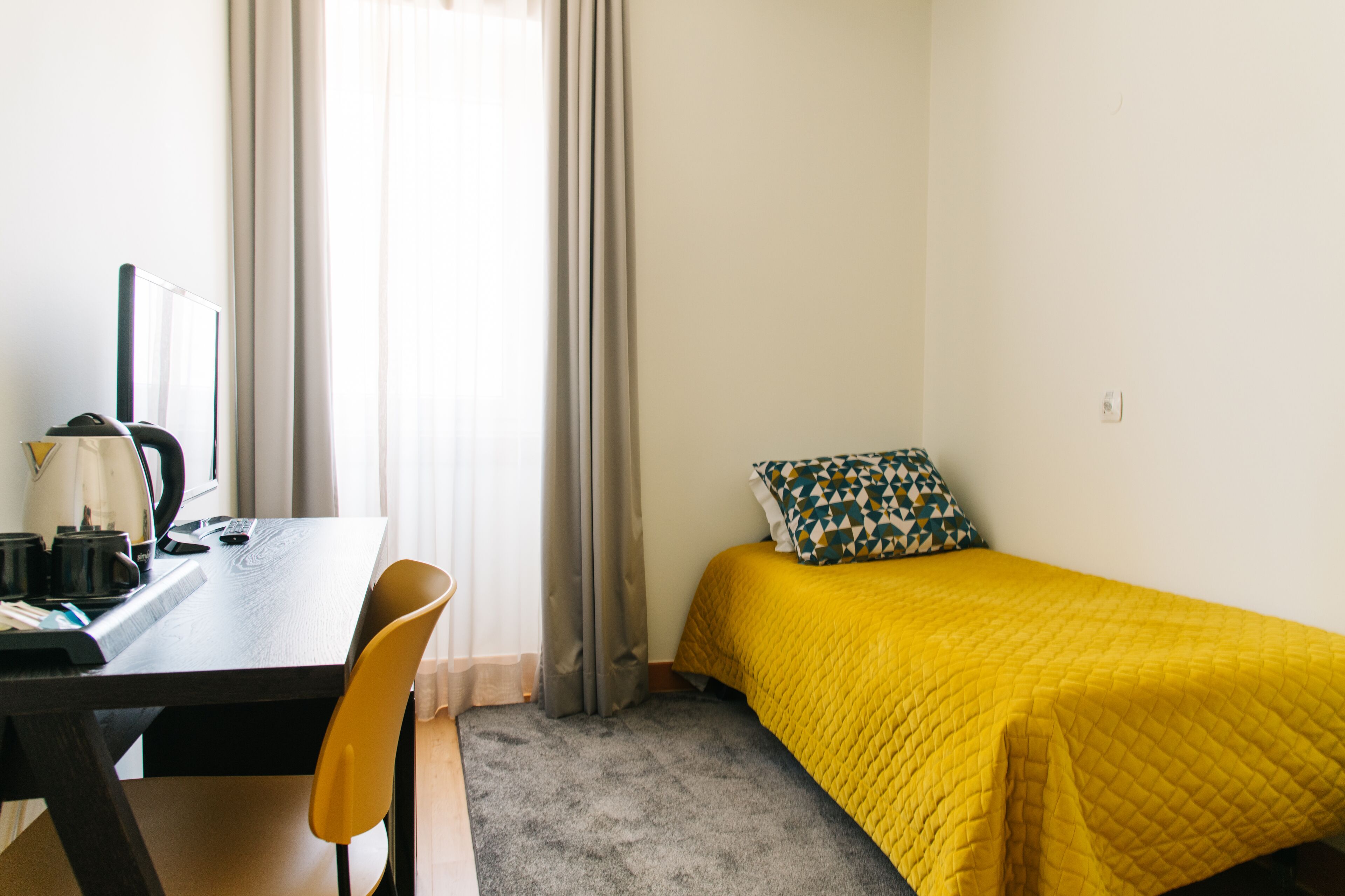 A small room with a desk, chair, and a bed with a yellow bedspread.