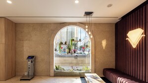 Un vestíbulo moderno con una balanza digital, un mostrador de recepción, un área de estar y un amplio ventanal de arco que ofrece vistas a la calle.