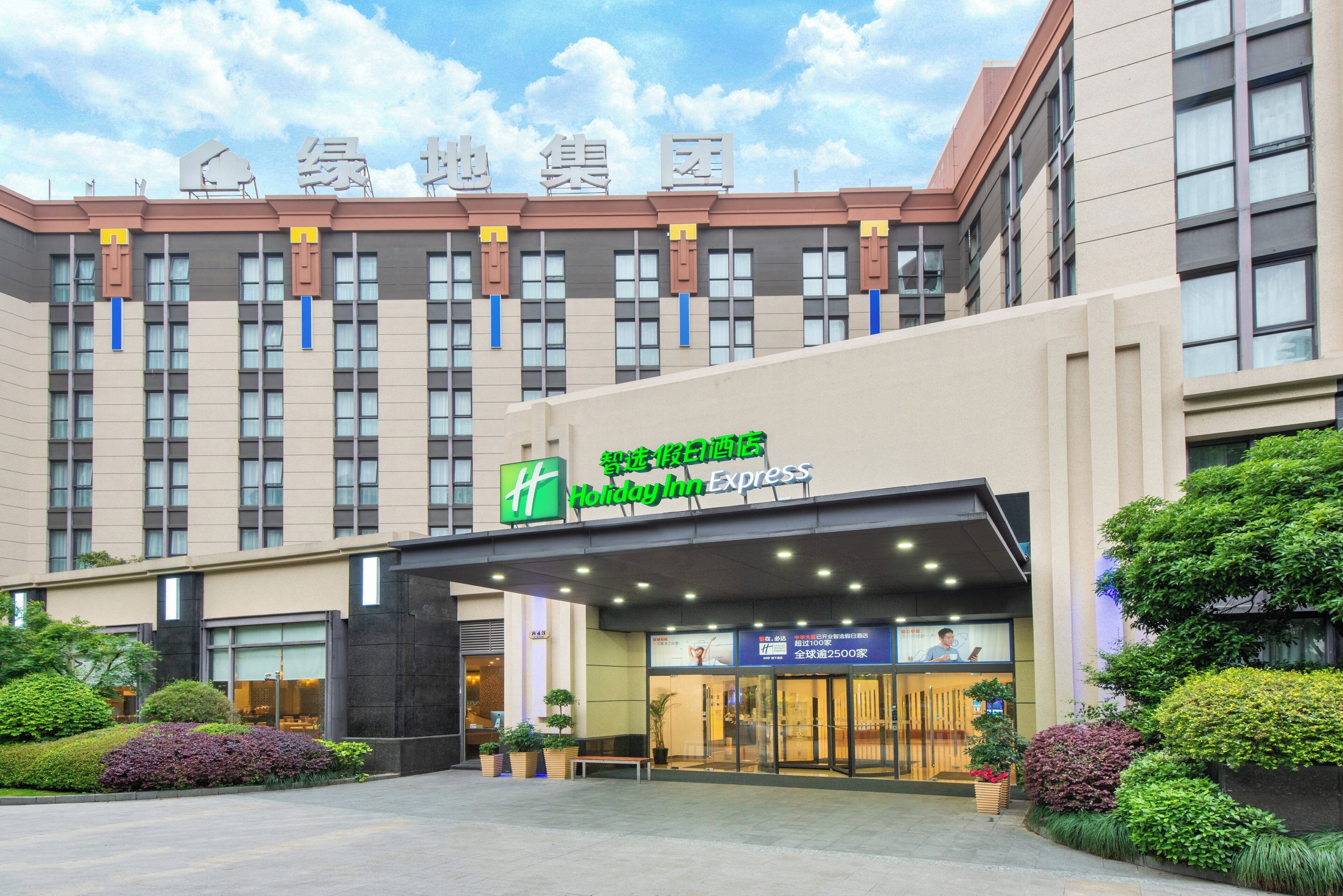 Un hotel Holiday Inn Express con una fachada moderna, grandes ventanales y un área de entrada bien cuidada con plantas en macetas.