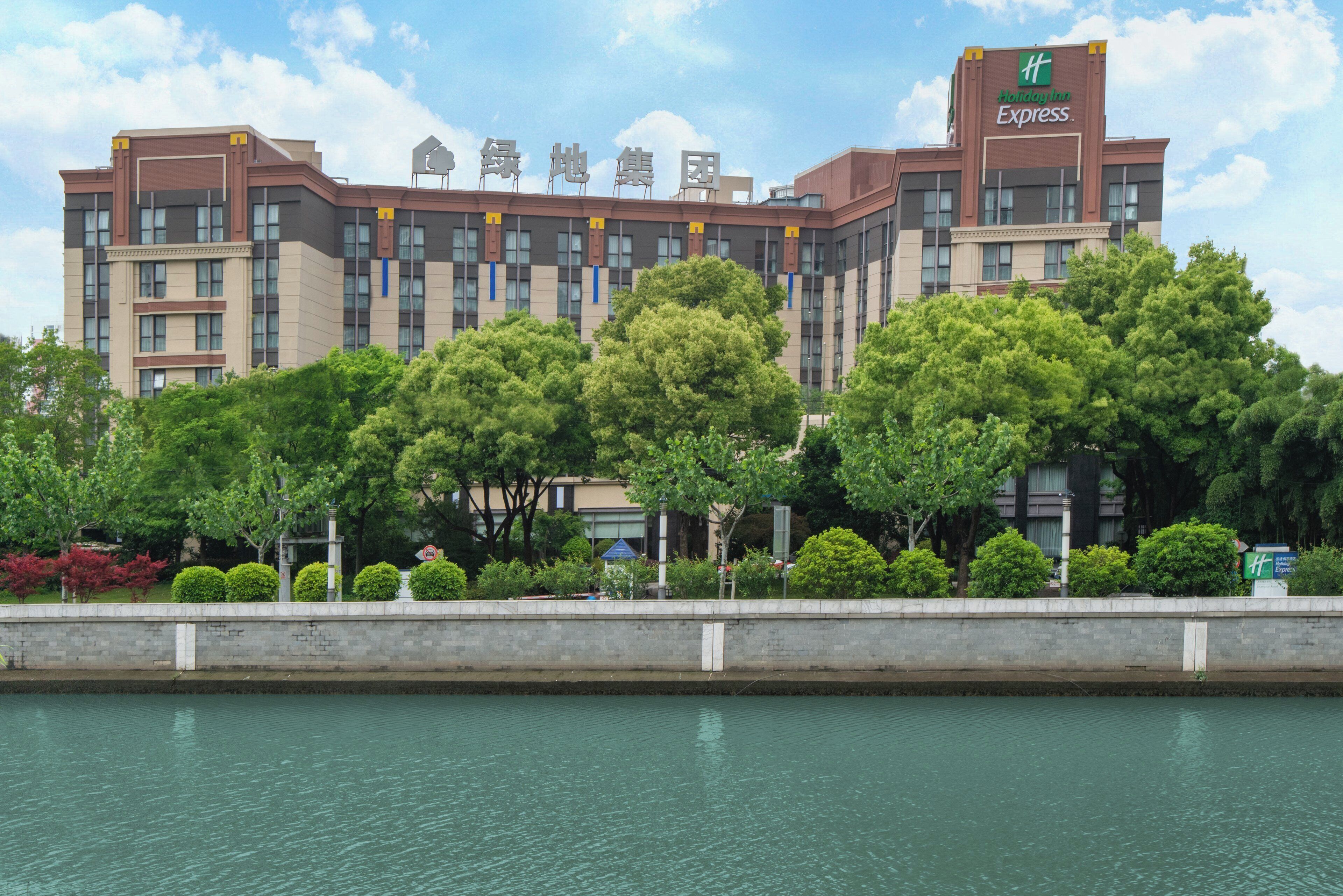 A multi-story hotel with a Holiday Inn Express sign, surrounded by lush greenery and a body of water in the foreground.
