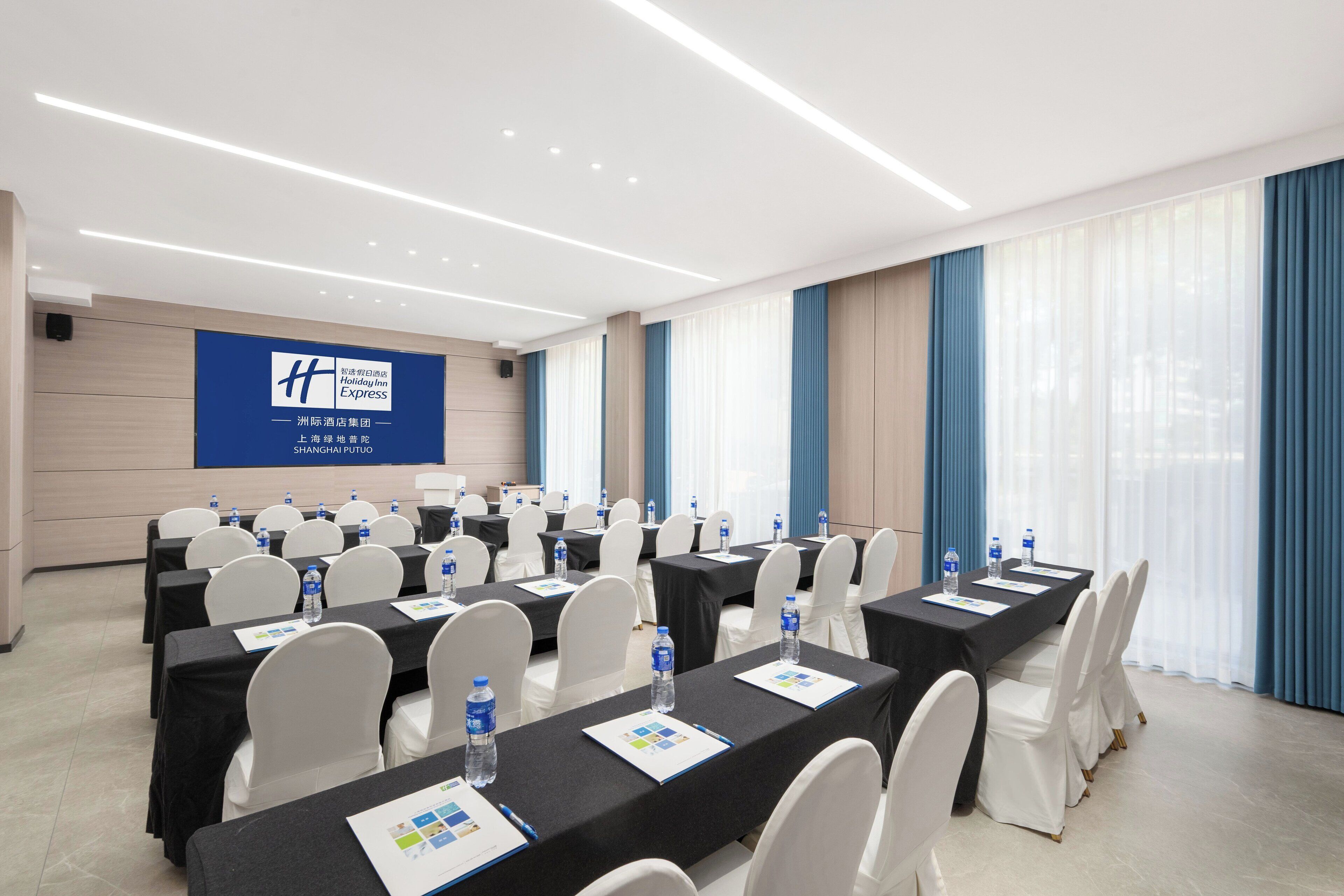 A conference room with multiple tables, white chairs, and water bottles.