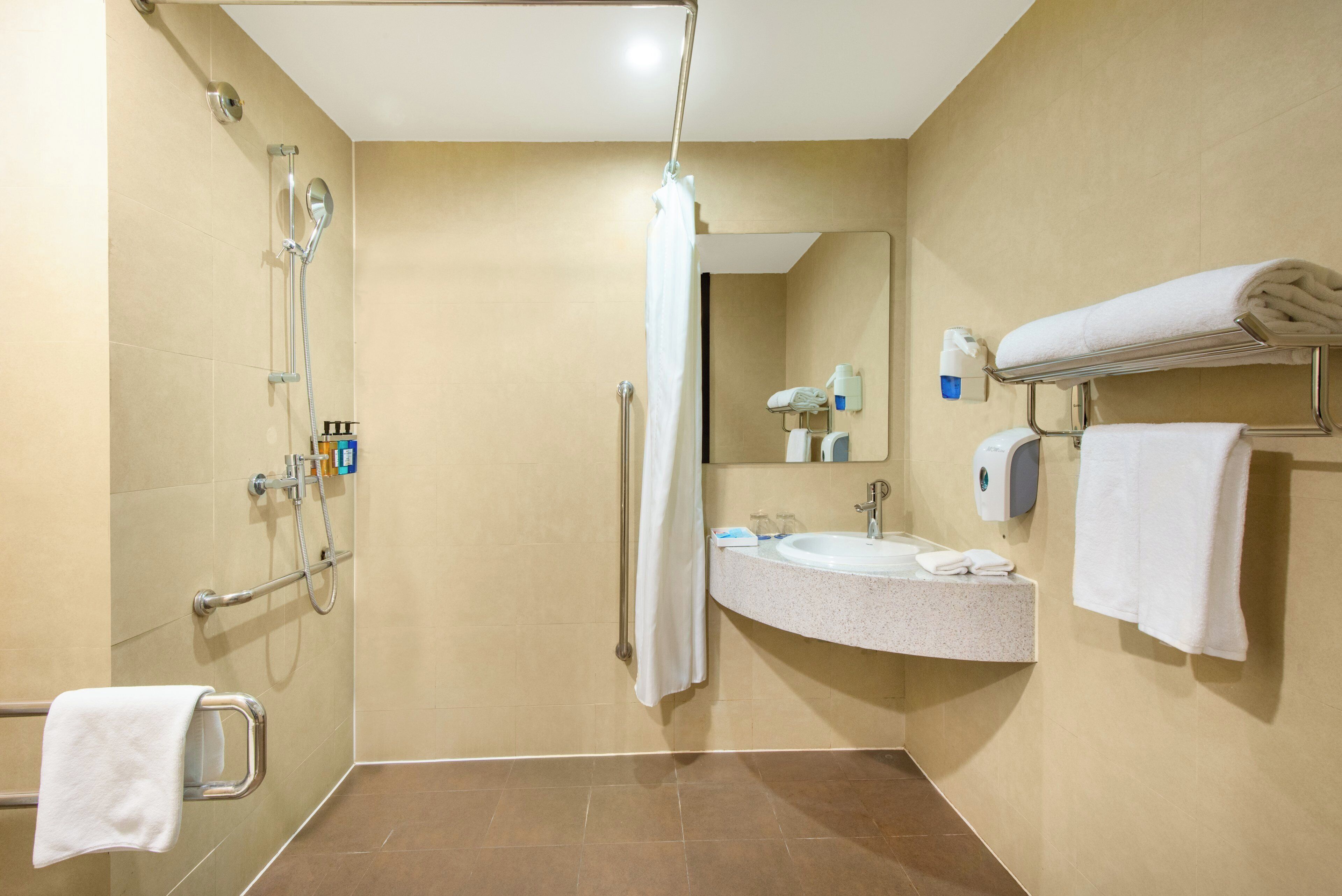 A hotel bathroom with a shower, a sink, a mirror, and a towel rack.