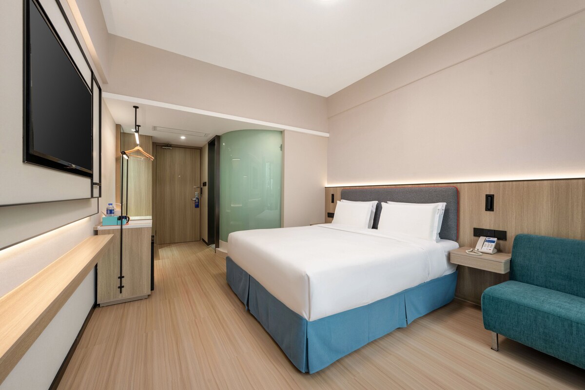 A modern hotel room with a large bed, a desk, a TV, and a seating area.