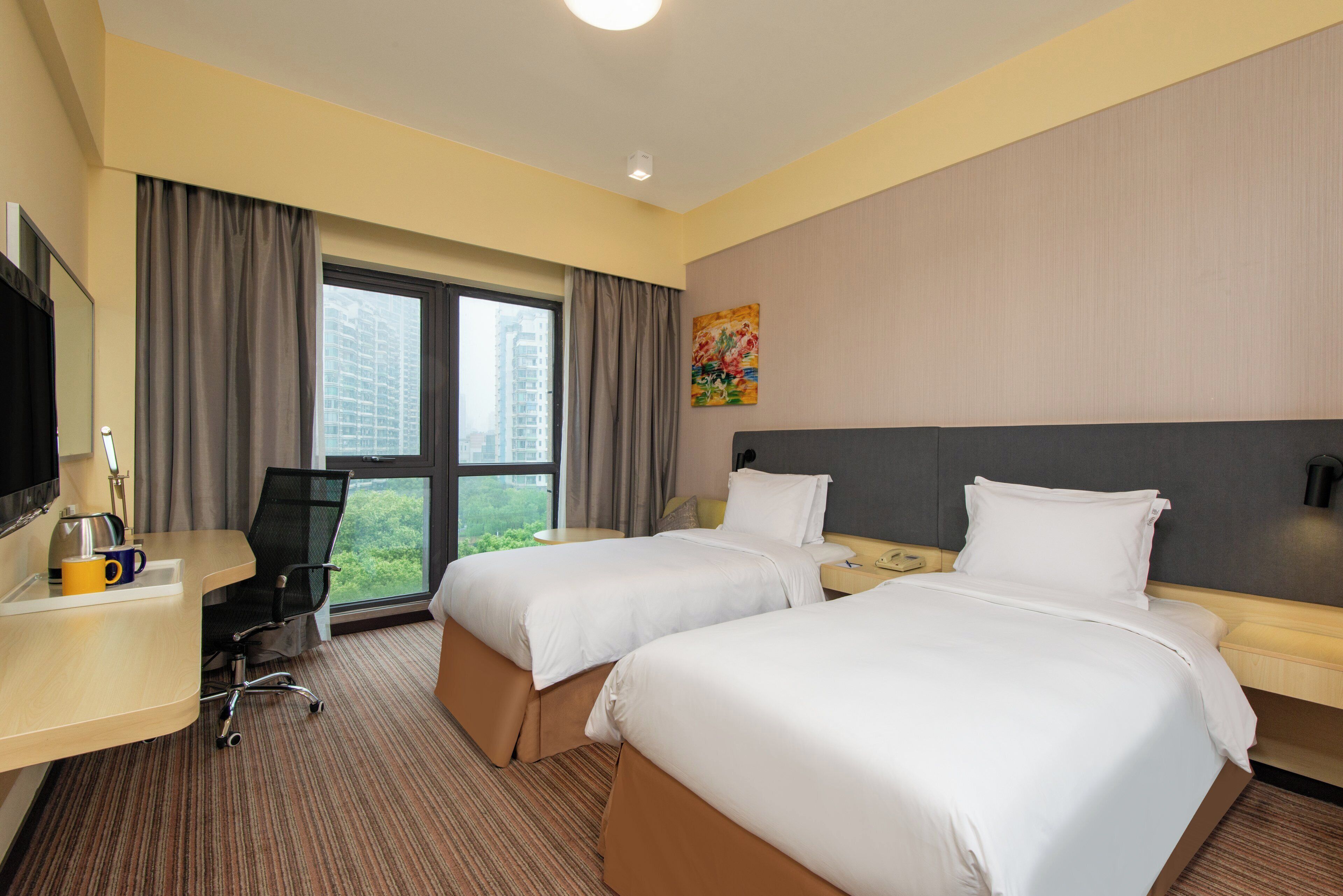 A hotel room with two beds, a desk with a chair, a television, and a window with curtains.