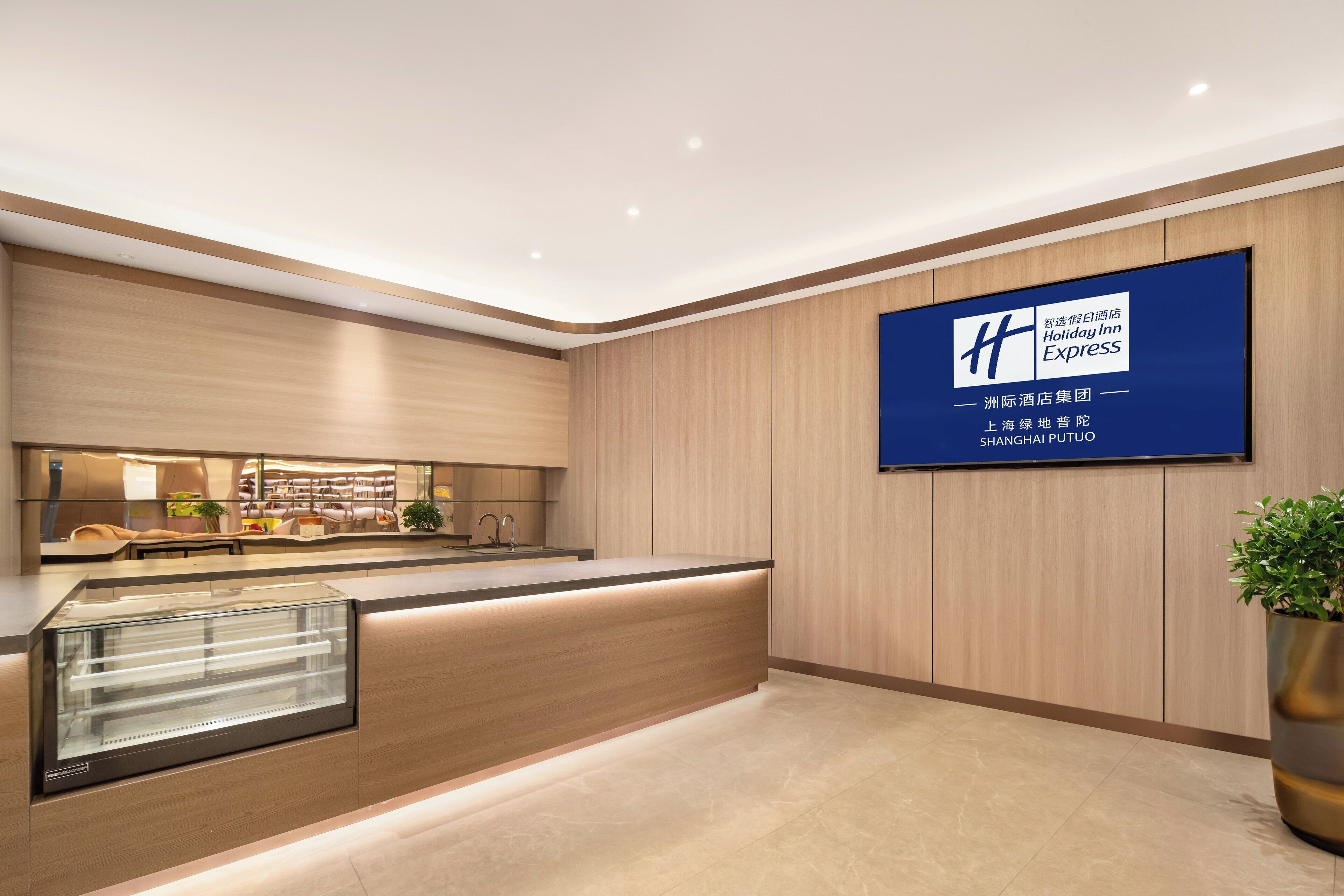 A modern hotel lobby with a reception desk, a large digital display, and a plant.