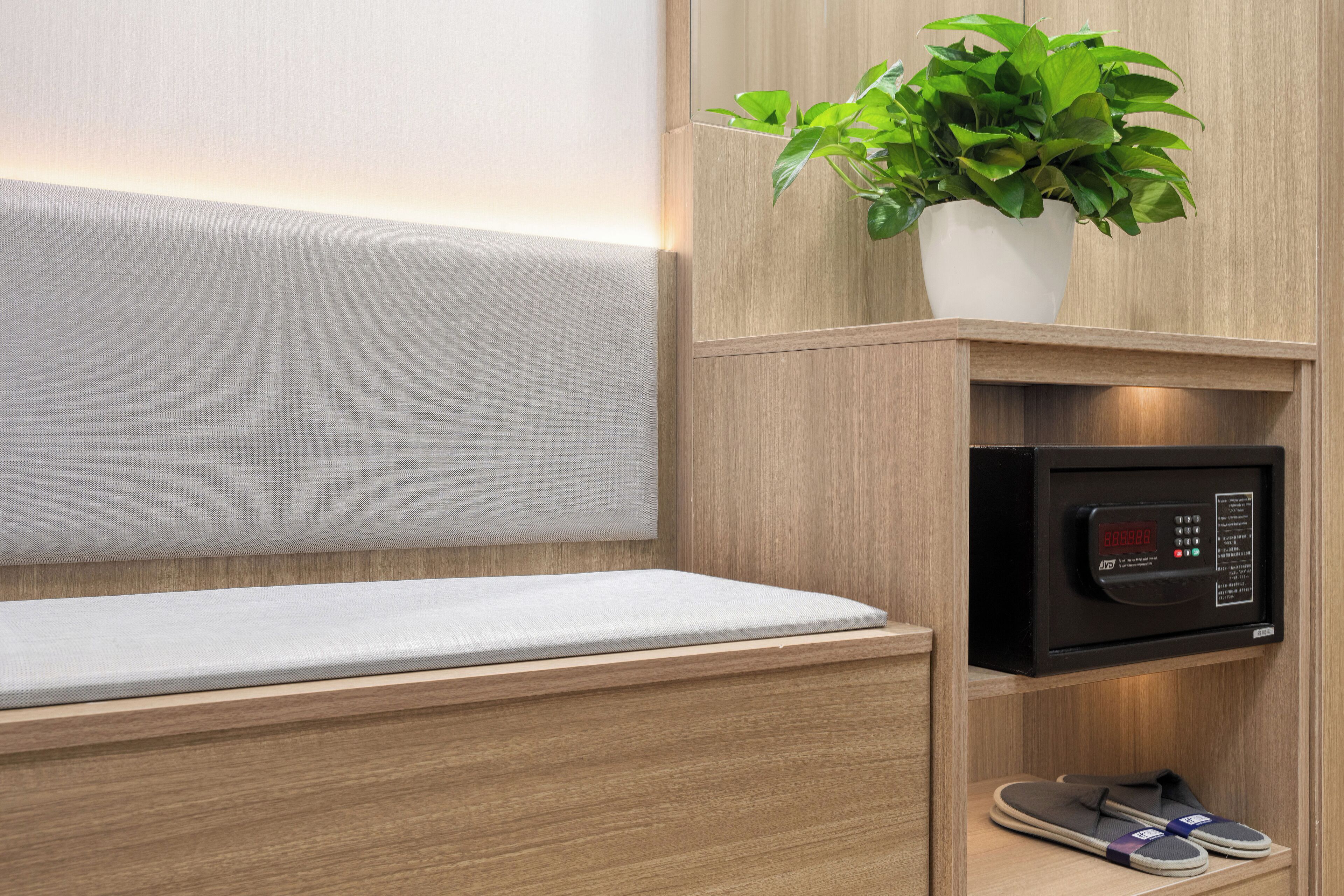 Une chambre d’hôtel avec un lit, une horloge numérique, une plante et une paire de chaussons.