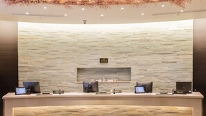 A reception desk with a stone wall backdrop, two computer monitors, a sign reading "WHG", and two wooden stools. - Hotel Gracery Ginza (Tokyo)