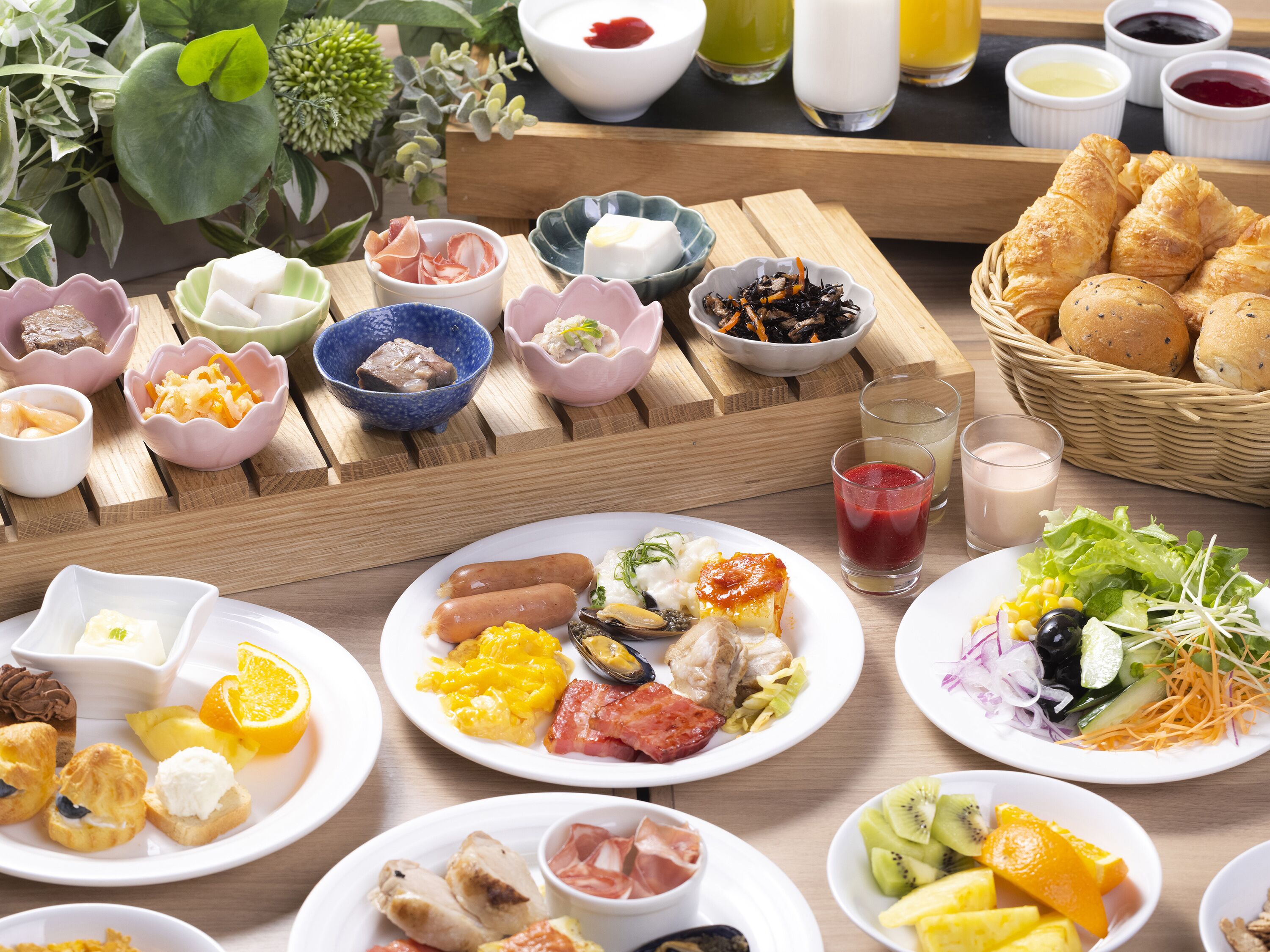 A breakfast buffet with various dishes, including pastries, meats, and fruits, arranged on a wooden table.