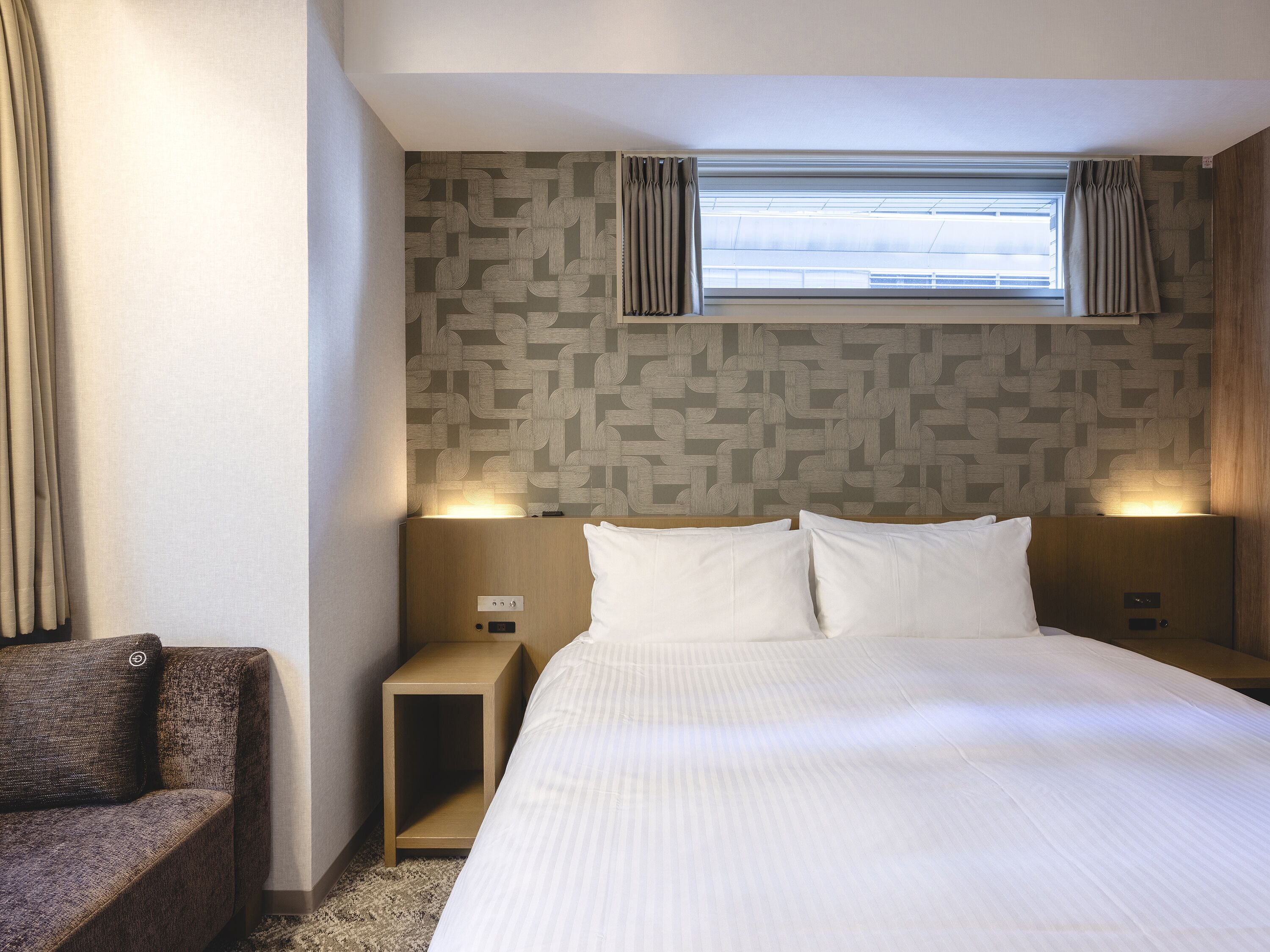 Une chambre d’hôtel avec un lit, une table de chevet, une chaise et une fenêtre avec des rideaux.