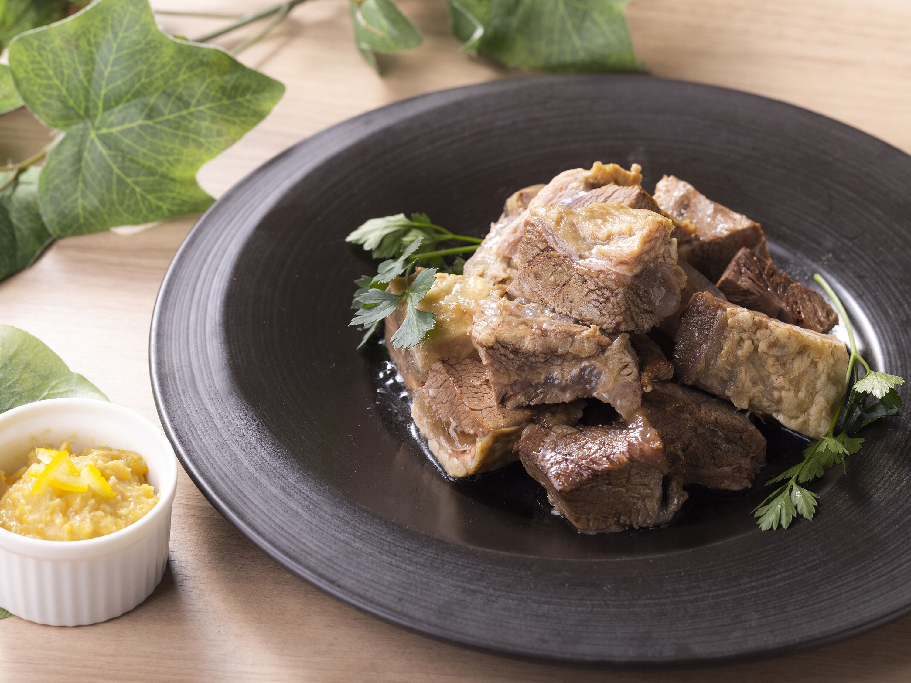 A plate of cooked meat with a garnish, accompanied by a small bowl of sauce.