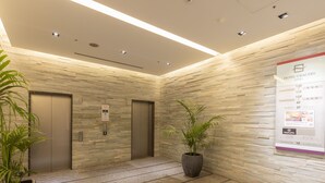 A hotel lobby with a modern design, featuring a reception desk, two elevators, and a large potted plant. - Hotel Gracery Ginza (Tokyo)