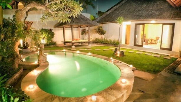A swimming pool with a circular design, surrounded by a stone deck and illuminated by small lights.