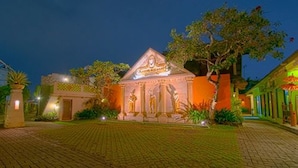 A building with a central statue, surrounded by a paved area and greenery.